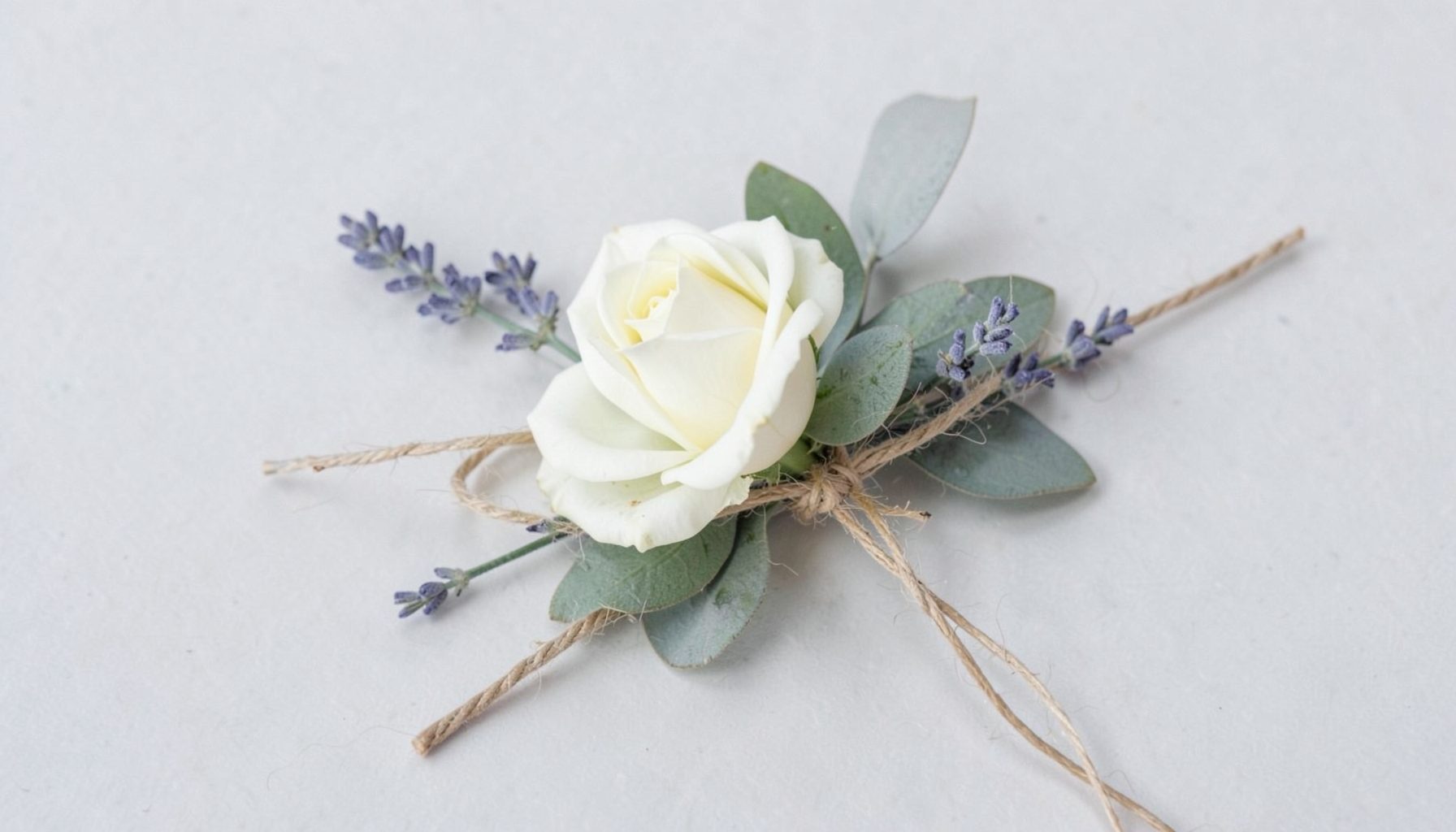 Boutonniere with a single ivory rose, sprig of lavender, and eucalyptus wrapped in twine