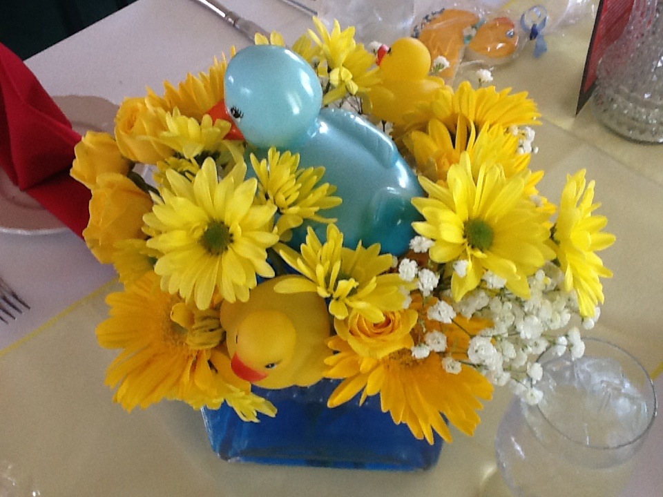 Yellow daisy and rose arrangement with baby's breath decorated with blue and yellow rubber duck figurines in a blue glass vase